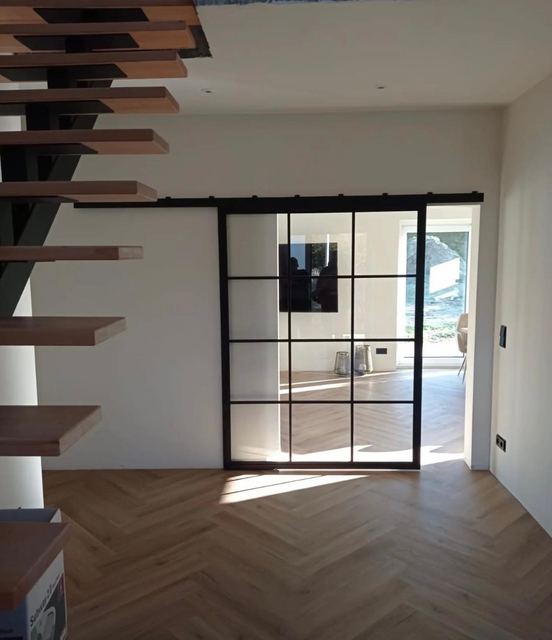 Schwarze Loft-Schiebetür an einer Laufschiene neben einer Treppe